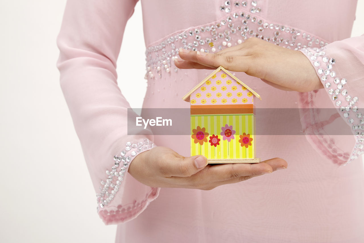 Midsection of woman holding model home against white background