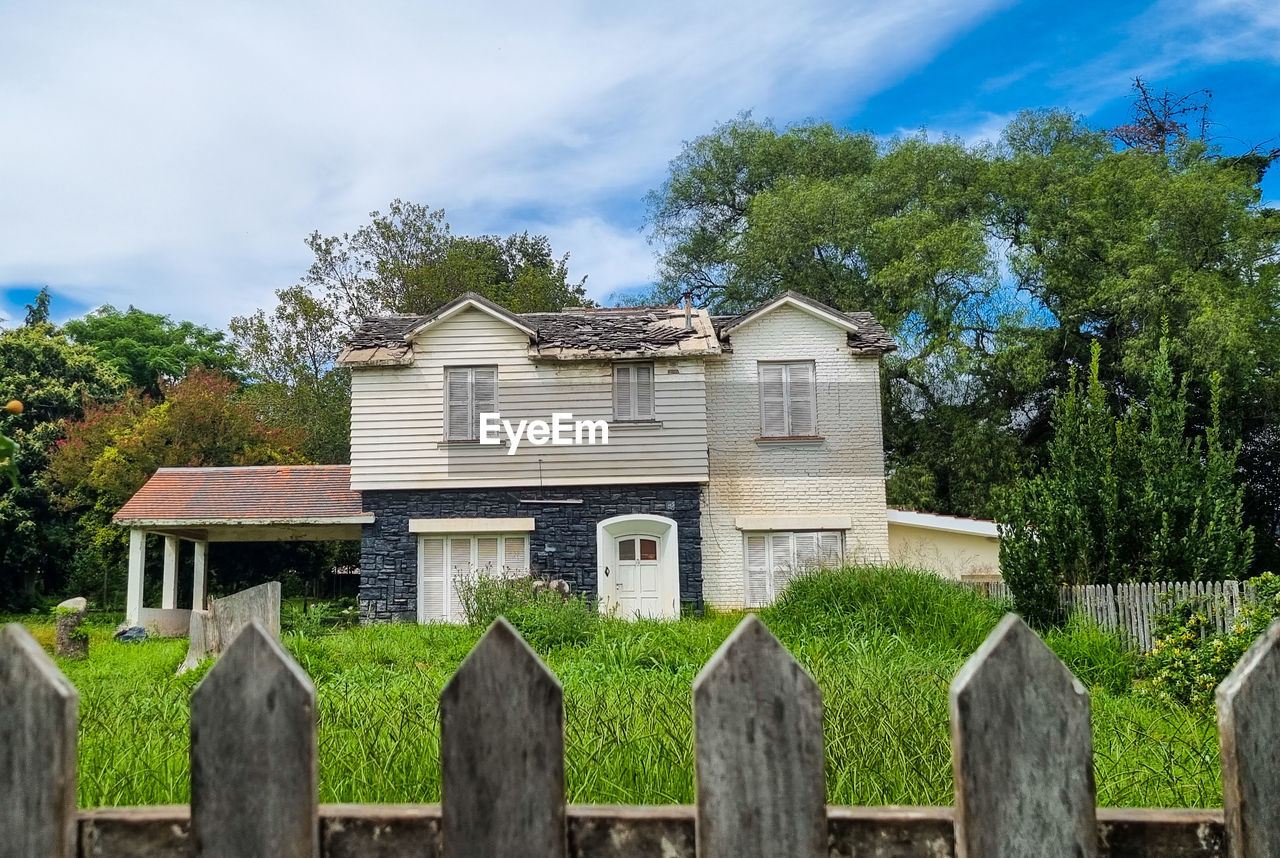 architecture, built structure, plant, building exterior, building, cloud, house, tree, sky, estate, wood, fence, nature, rural area, residential district, no people, home, grass, rural scene, landscape, outdoors, picket fence, front or back yard, day, mansion, residential area, gate, green, home ownership, home fencing