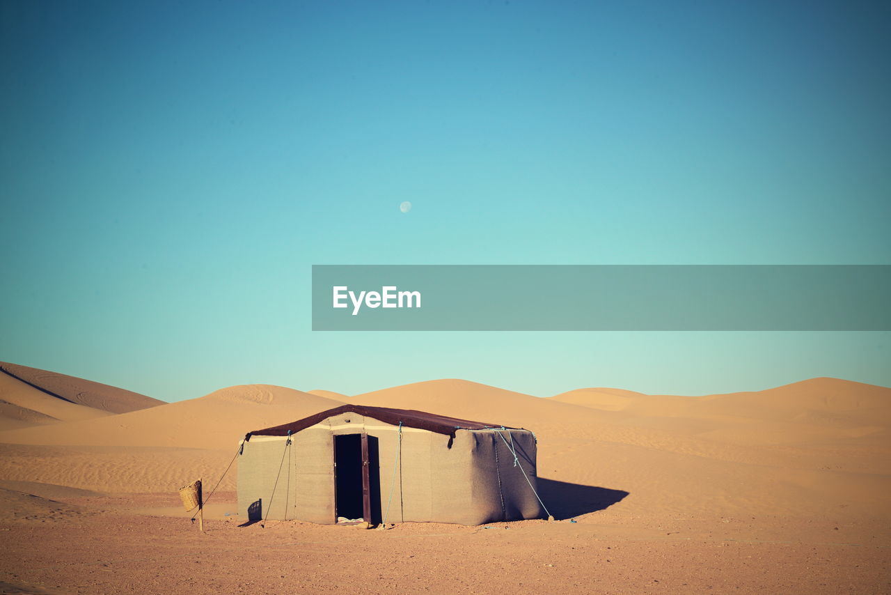 Scenic view of hut on sand dunes in desert against clear sky