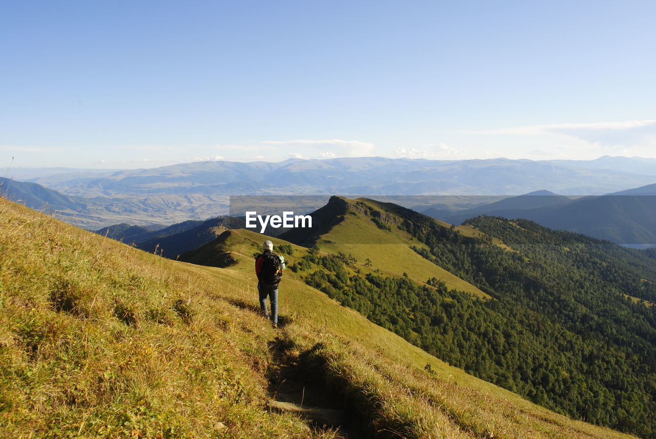 Rear view of hiker standing on grassy mountain against sky