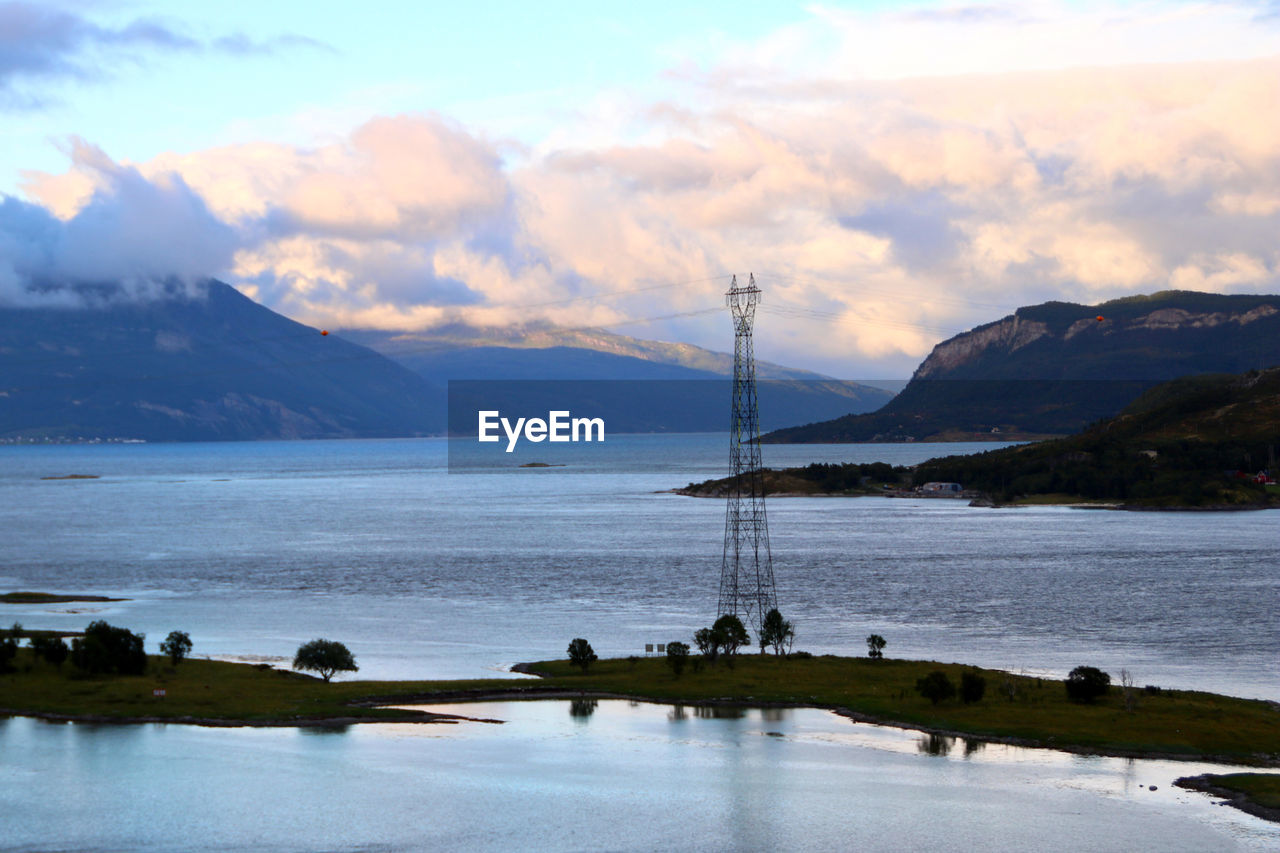 Scenic view of sea and power lines against sky at sunset