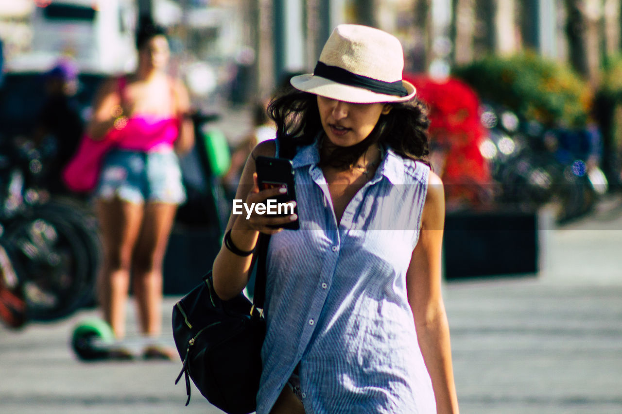 MIDSECTION OF WOMAN HOLDING SMART PHONE WHILE STANDING ON CITY