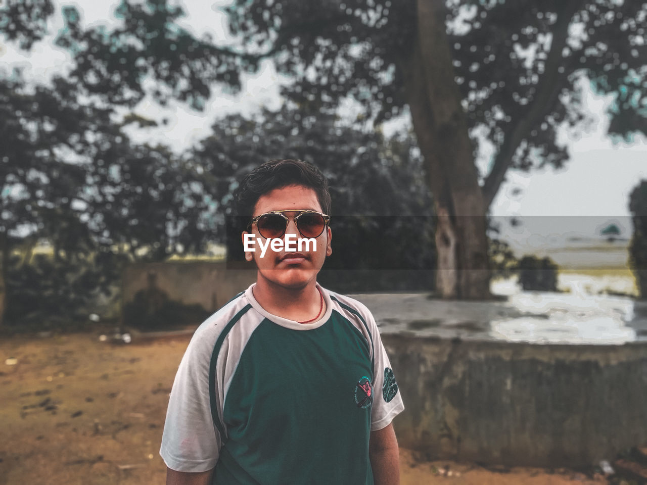 PORTRAIT OF MID ADULT MAN WEARING SUNGLASSES STANDING AGAINST TREES