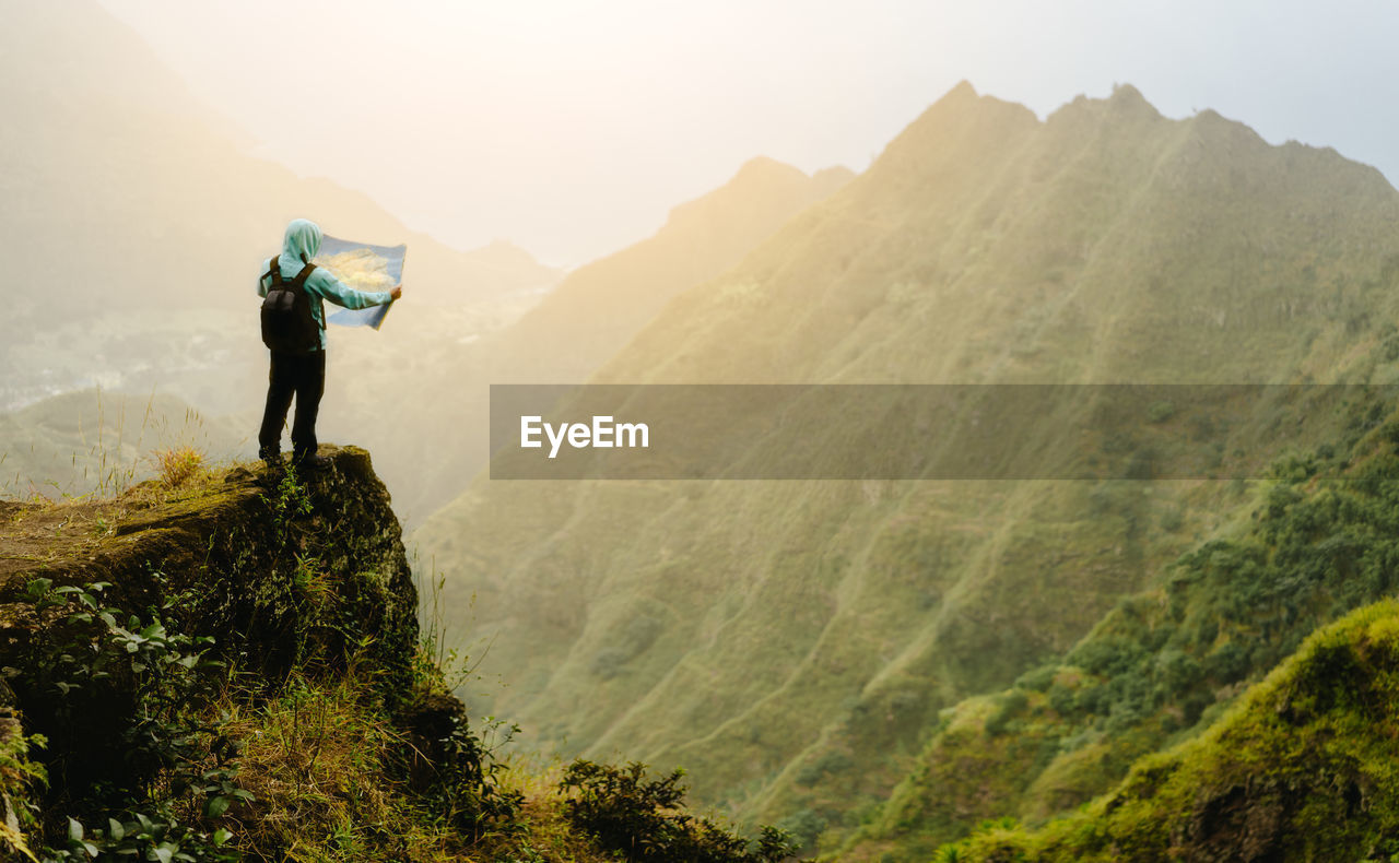 Rear view of man standing on mountain against sky