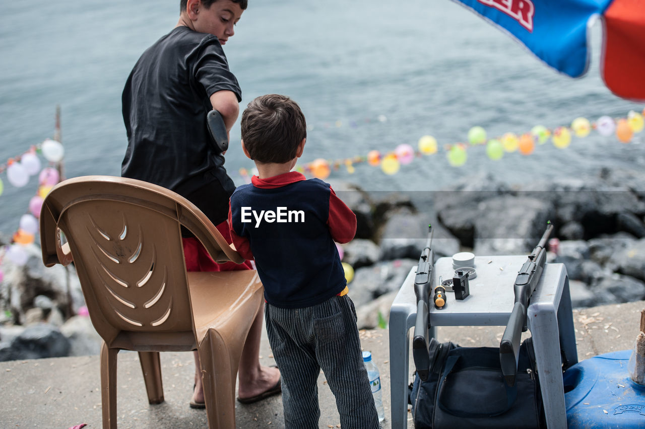 REAR VIEW OF FATHER WITH SON STANDING ON SEA