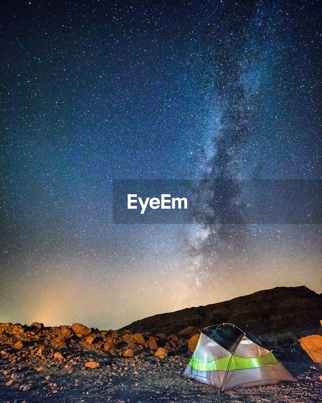 Tent by mountain against star field at night