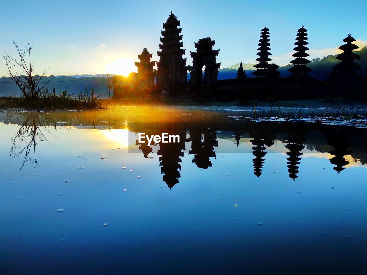 REFLECTION OF SILHOUETTE TREES IN LAKE AGAINST SKY AT SUNSET