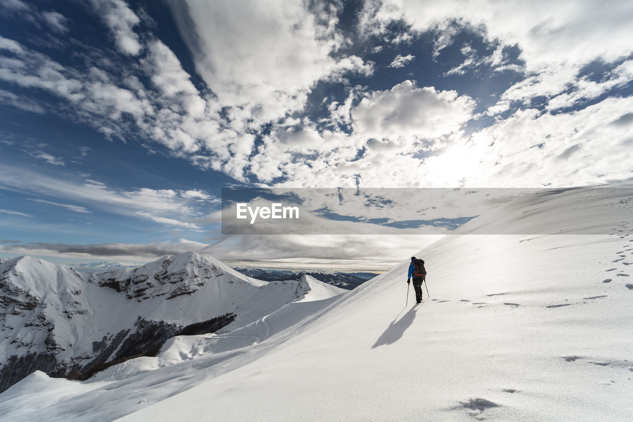 Mid adult man hiking on snowcapped mountain against cloudy sky