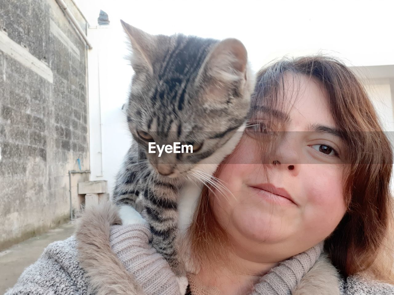 PORTRAIT OF WOMAN WITH CAT AGAINST WHITE WALL