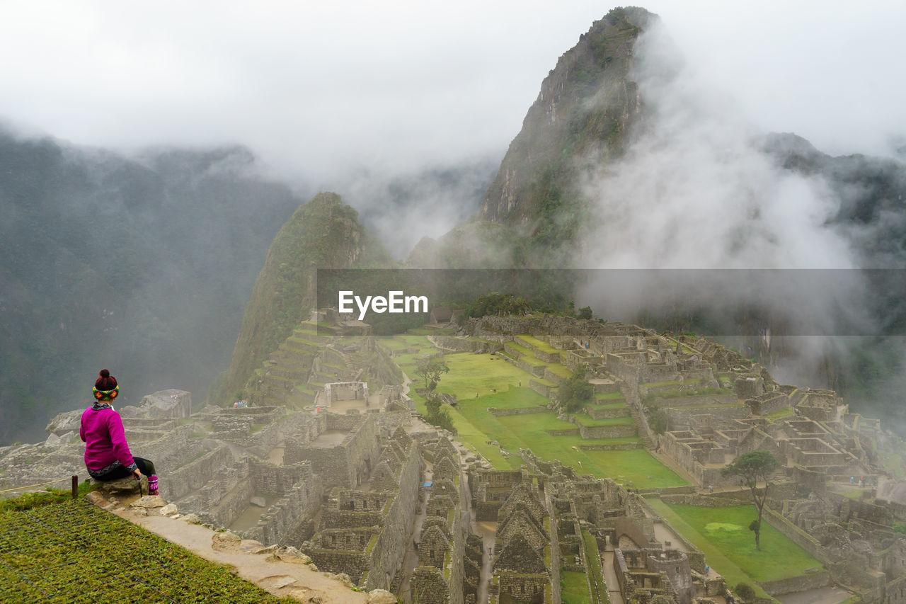 Rear view of woman sitting at machu picchu against sky
