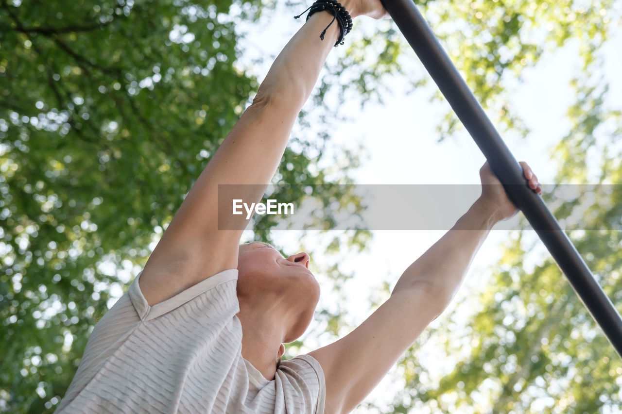 Low angle view of woman holding umbrella against trees