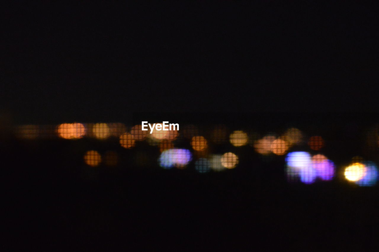 DEFOCUSED IMAGE OF ILLUMINATED CITYSCAPE AGAINST SKY