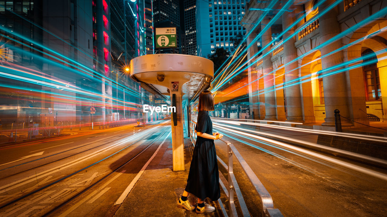 Woman standing amidst light trails on road at night