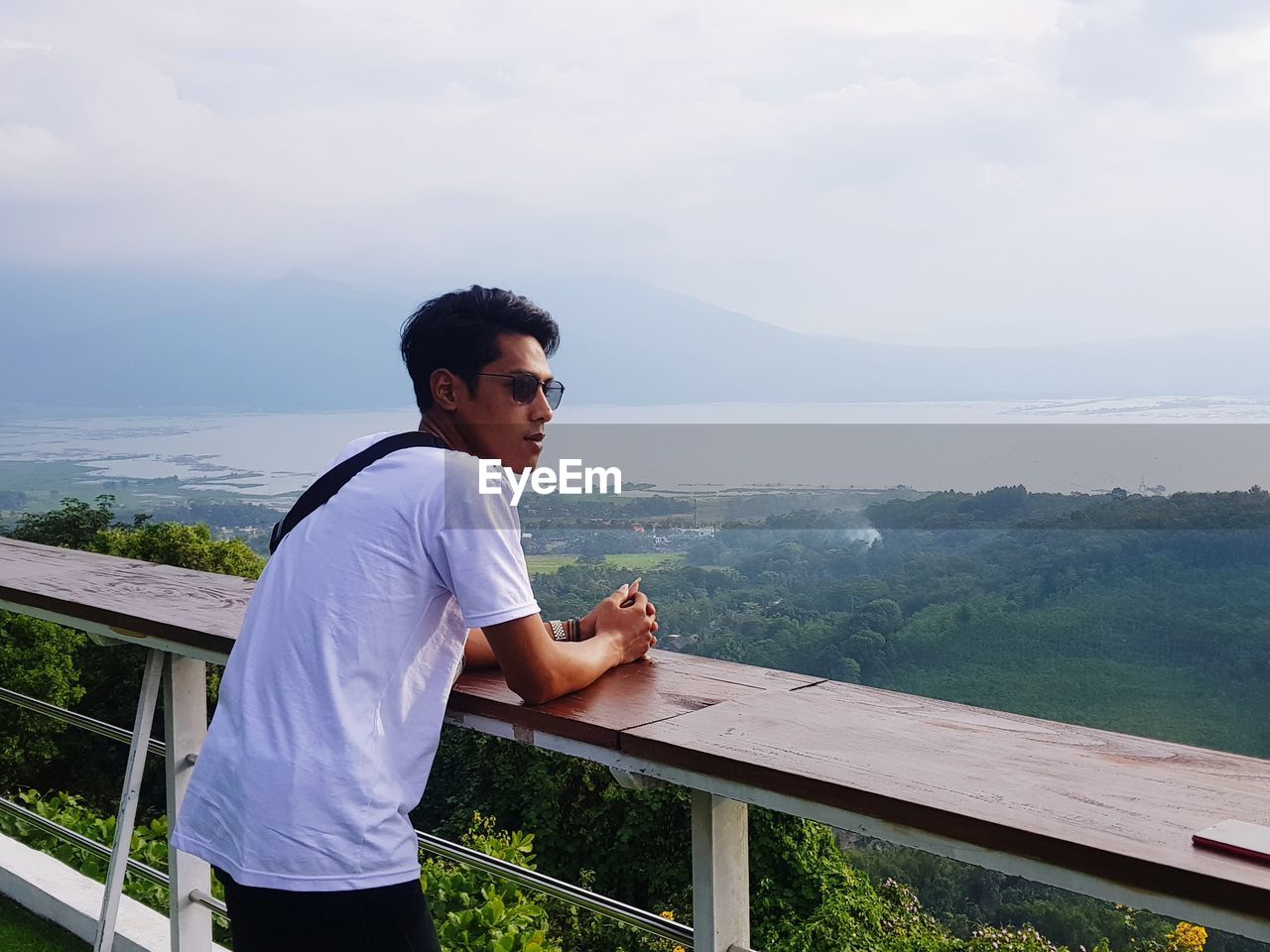 Side view of young man standing by railing against sea