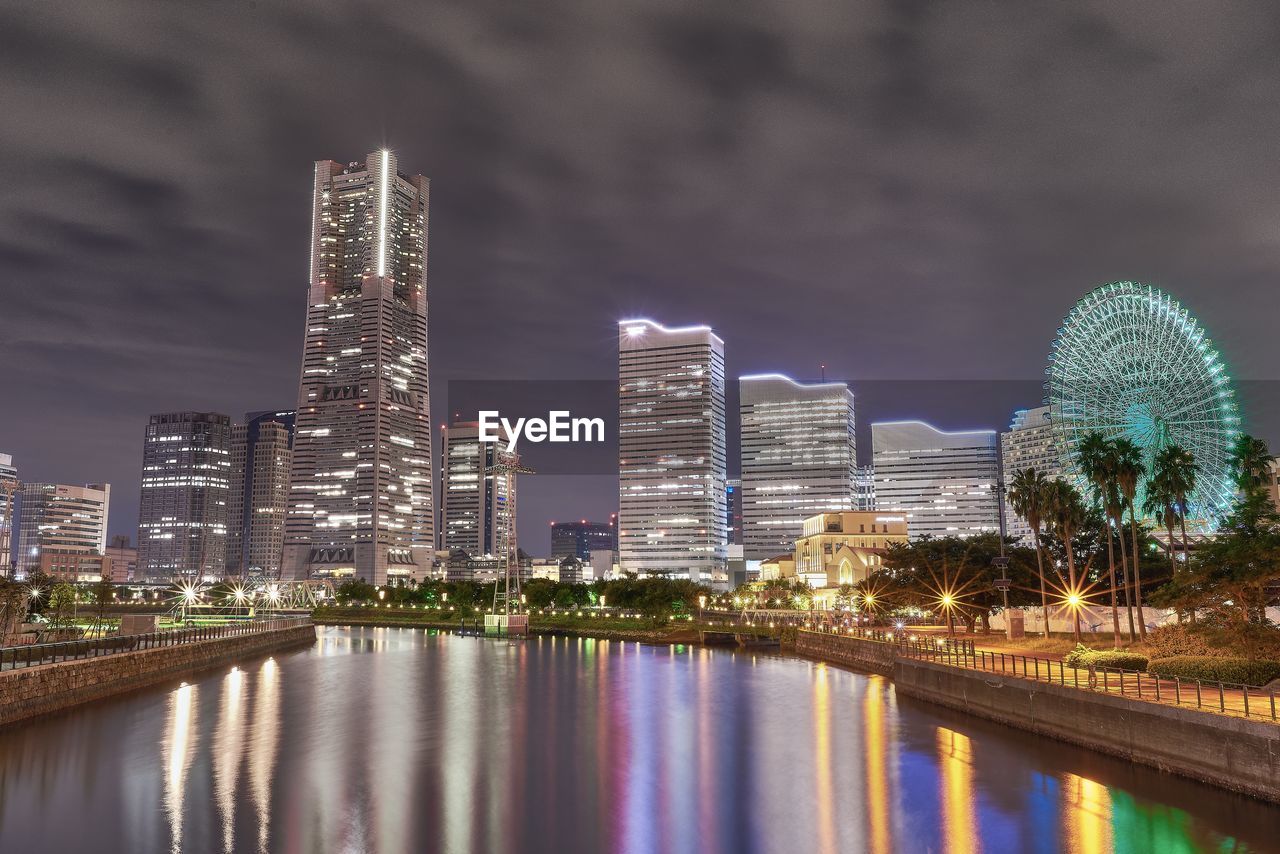 Illuminated modern buildings in city against sky at night