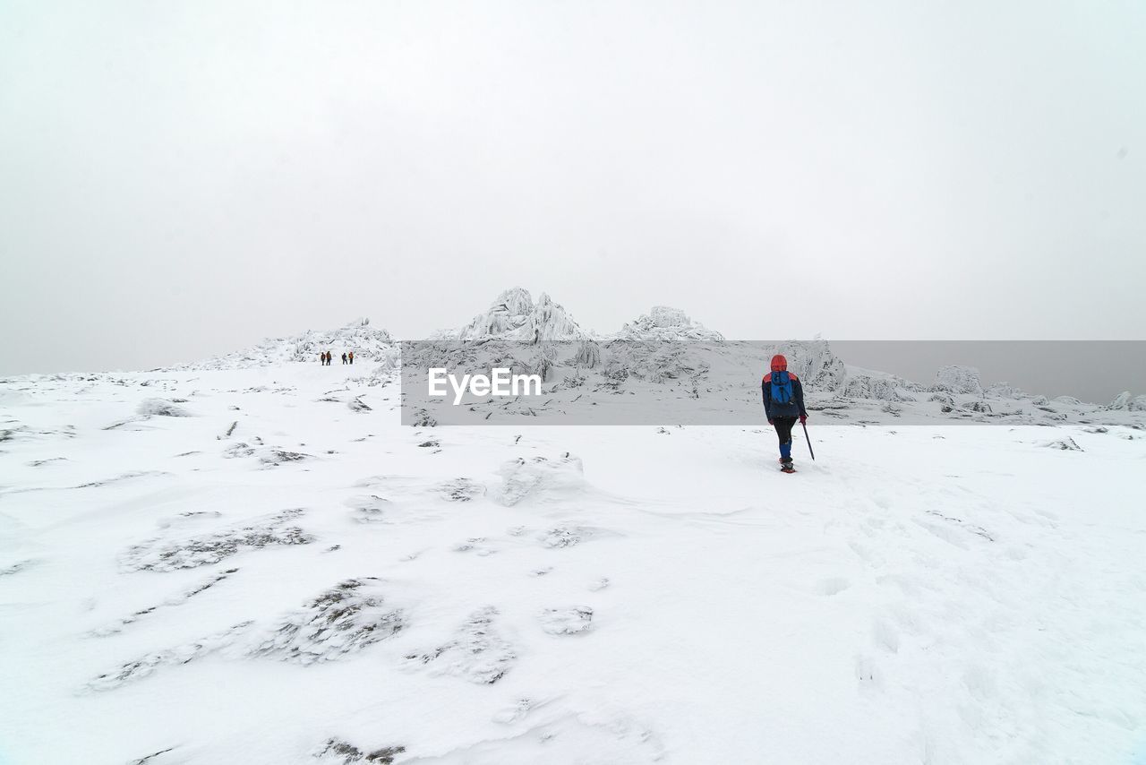 Rear view of person hiking on snowcapped mountain against sky