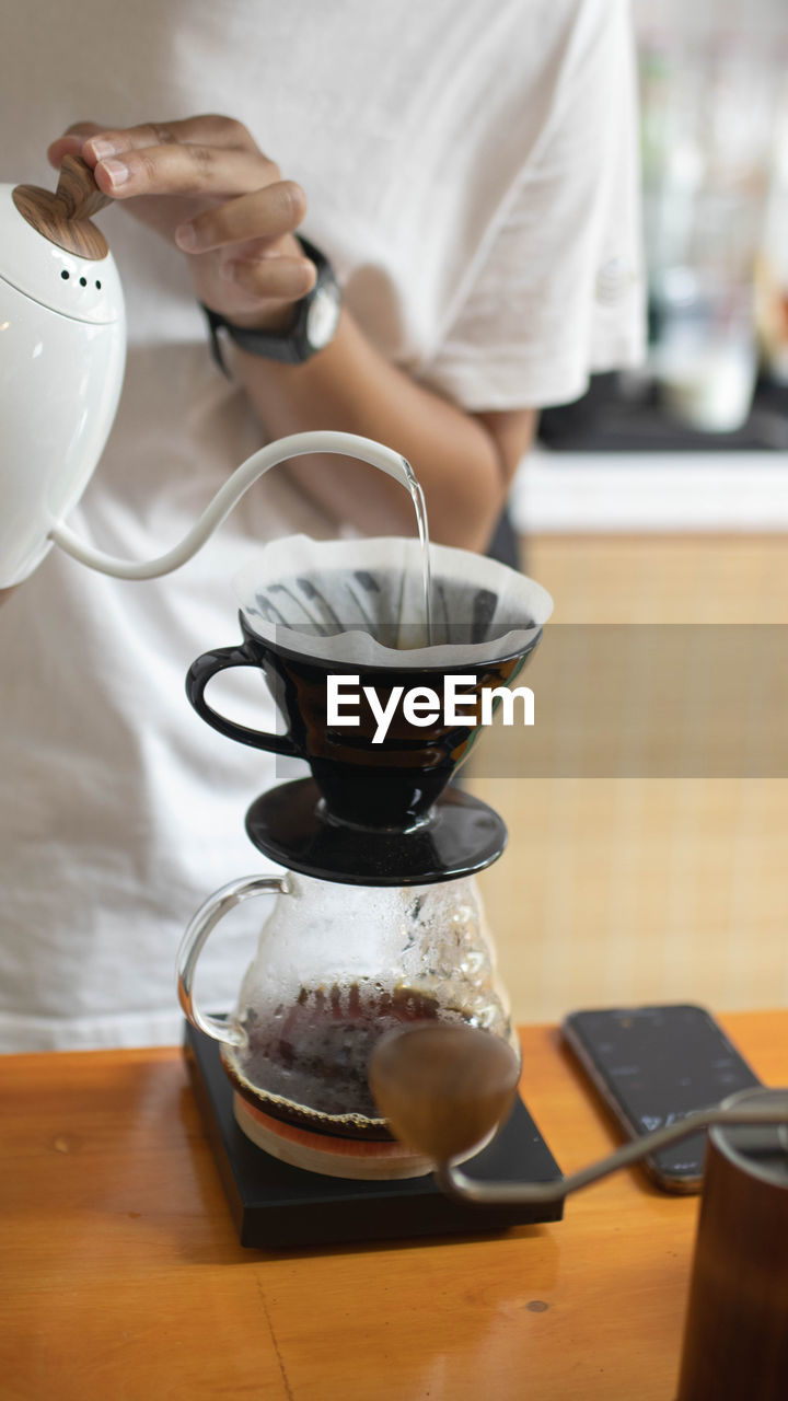 Barista is making drip brewing, filtered coffee with hot water and filter paper in coffee shop 