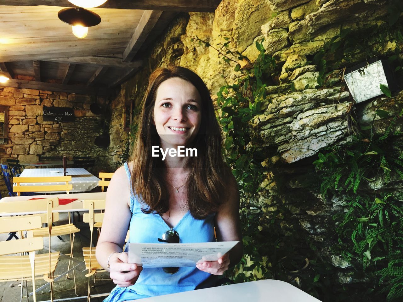 PORTRAIT OF A SMILING YOUNG WOMAN STANDING AGAINST WALL