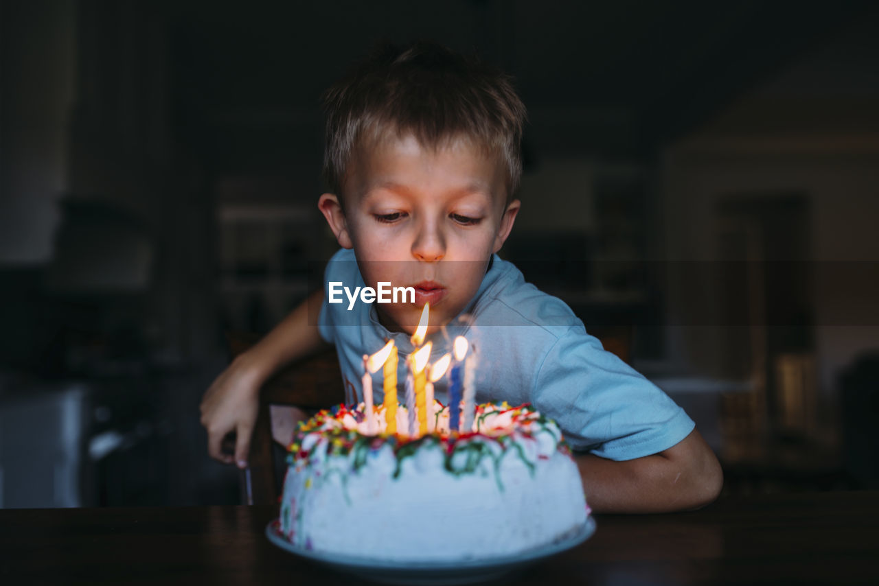 Boy blowing birthday candles in darkroom