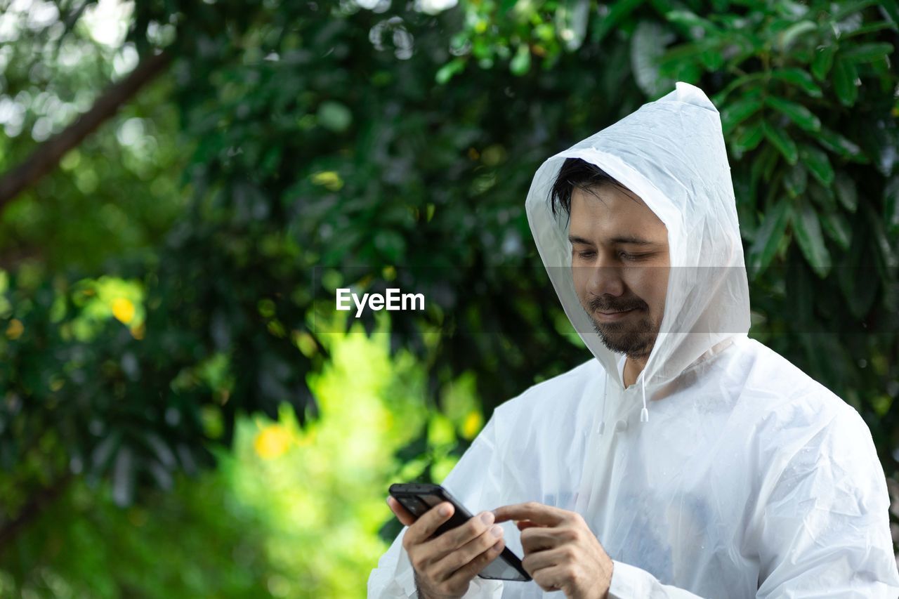 Asian man in a white raincoat using a smartphone outdoor
