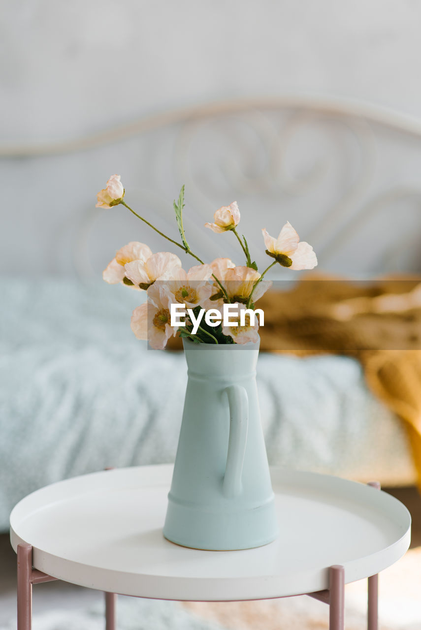 Artificial poppy flowers in a blue vase in the form of a jug on the coffee table in the interior