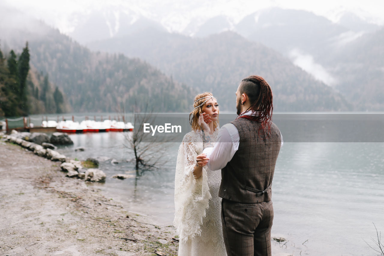 Happy newlyweds in love a man and a woman in wedding clothes embrace on the shore of the lake