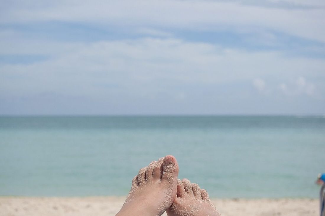 Close-up of human feet on beach by sea against sky