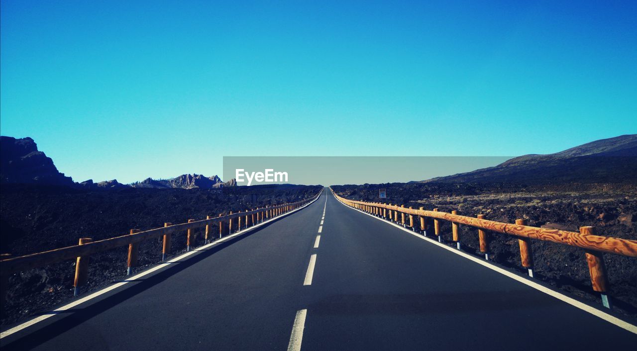 Empty road against clear blue sky