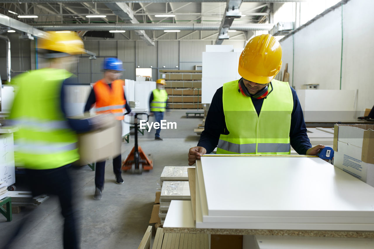 Worker examining wooden boards in factory with colleagues moving in background
