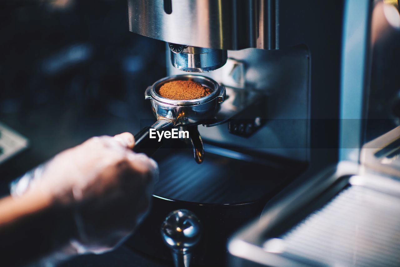 Cropped hand of person holding portafilter with ground coffee in cafe