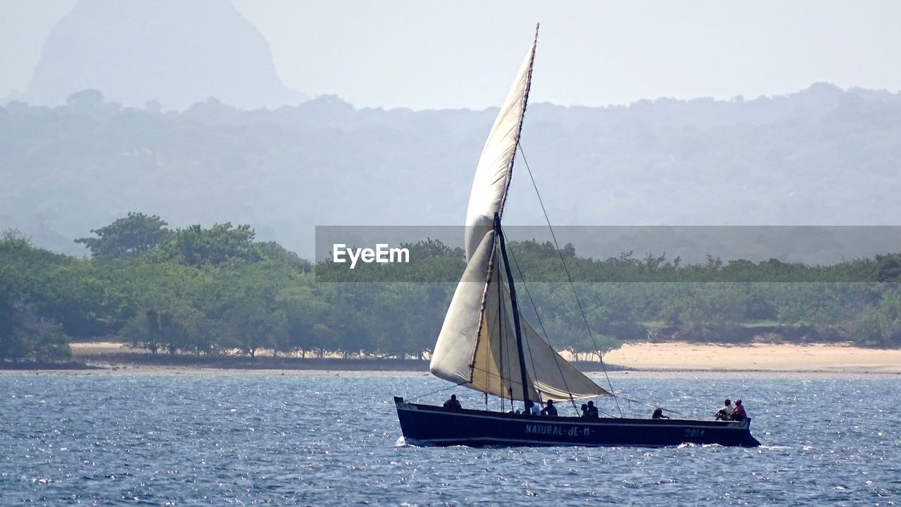 SAILBOAT SAILING ON RIVER BY MOUNTAIN