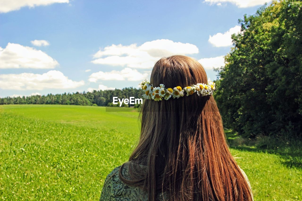 Rear view of woman wearing flowers while standing against sky