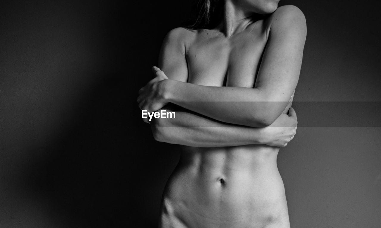 Midsection of naked young woman against black background