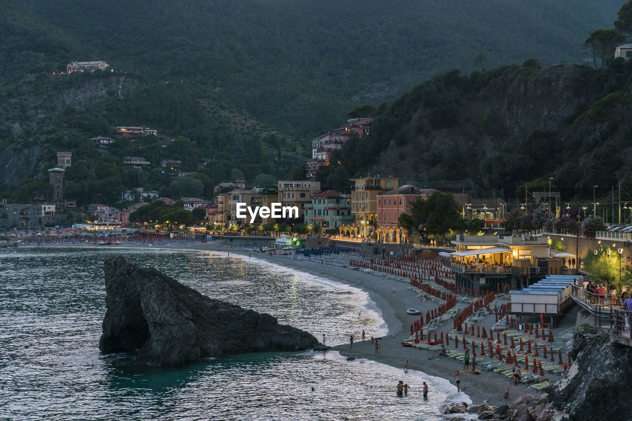 Aerial view of sandy beach with loungers and illuminated houses located between sea and mountain in evening on resort