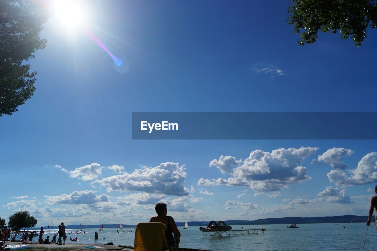 Rear view of woman relaxing on chair at beach against sky on sunny day