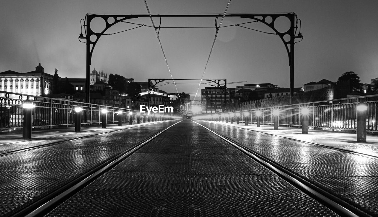 Black and white  perspective of rail track on portoportoilluminated  bridge by night. wet and foggy.