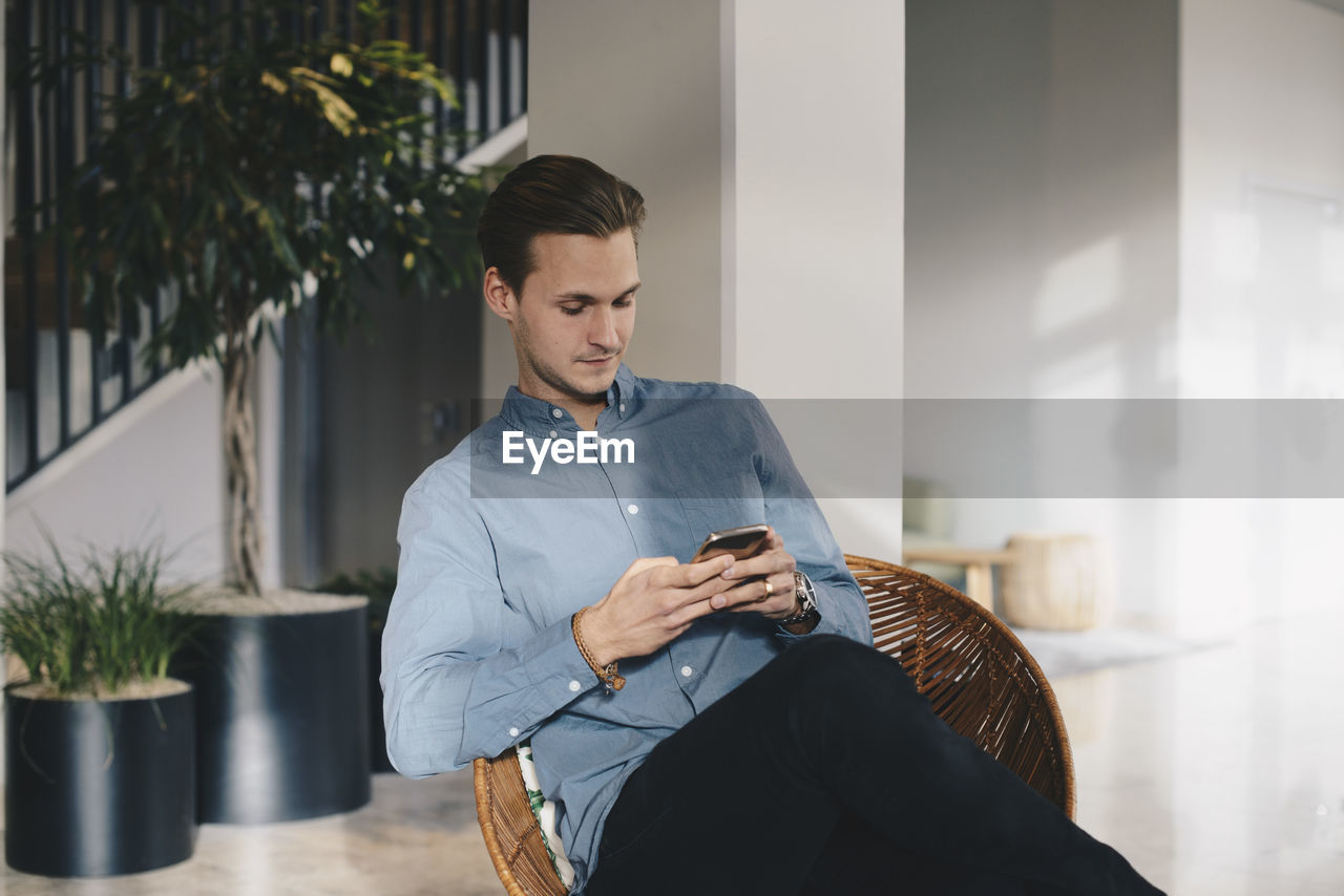 Businessman using smart phone while sitting on chair in office