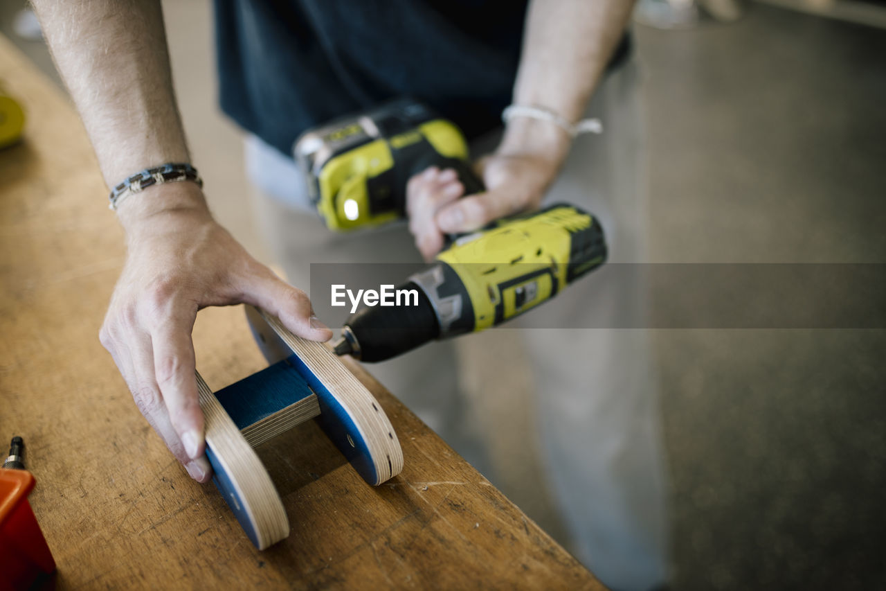 Craftsman making hole in wood material with drill machine on table at workshop