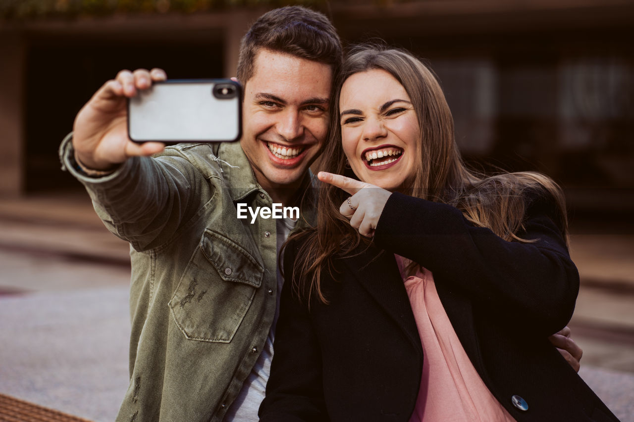 Boyfriend taking selfie with girlfriend over mobile phone outdoors