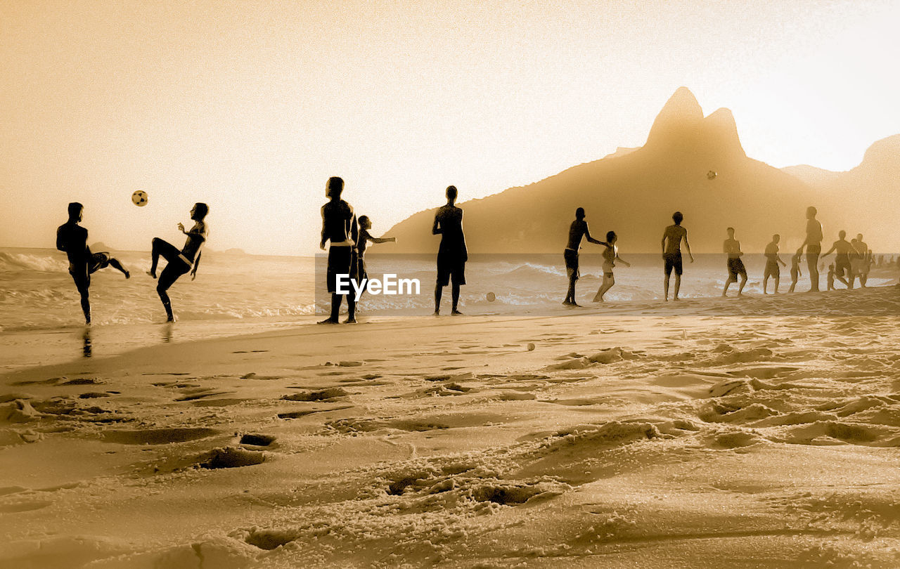 People playing soccer at beach against clear sky