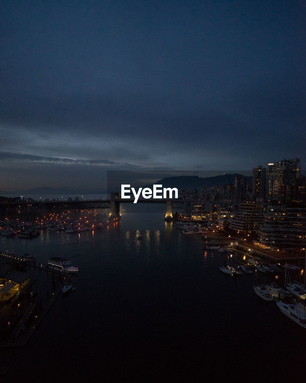 Illuminated city by sea against sky at dusk