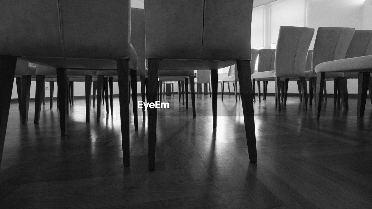 black and white, seat, black, monochrome, indoors, chair, monochrome photography, flooring, white, architecture, no people, absence, table, light, floor, empty, in a row, wood, furniture, built structure, hardwood floor, darkness, building