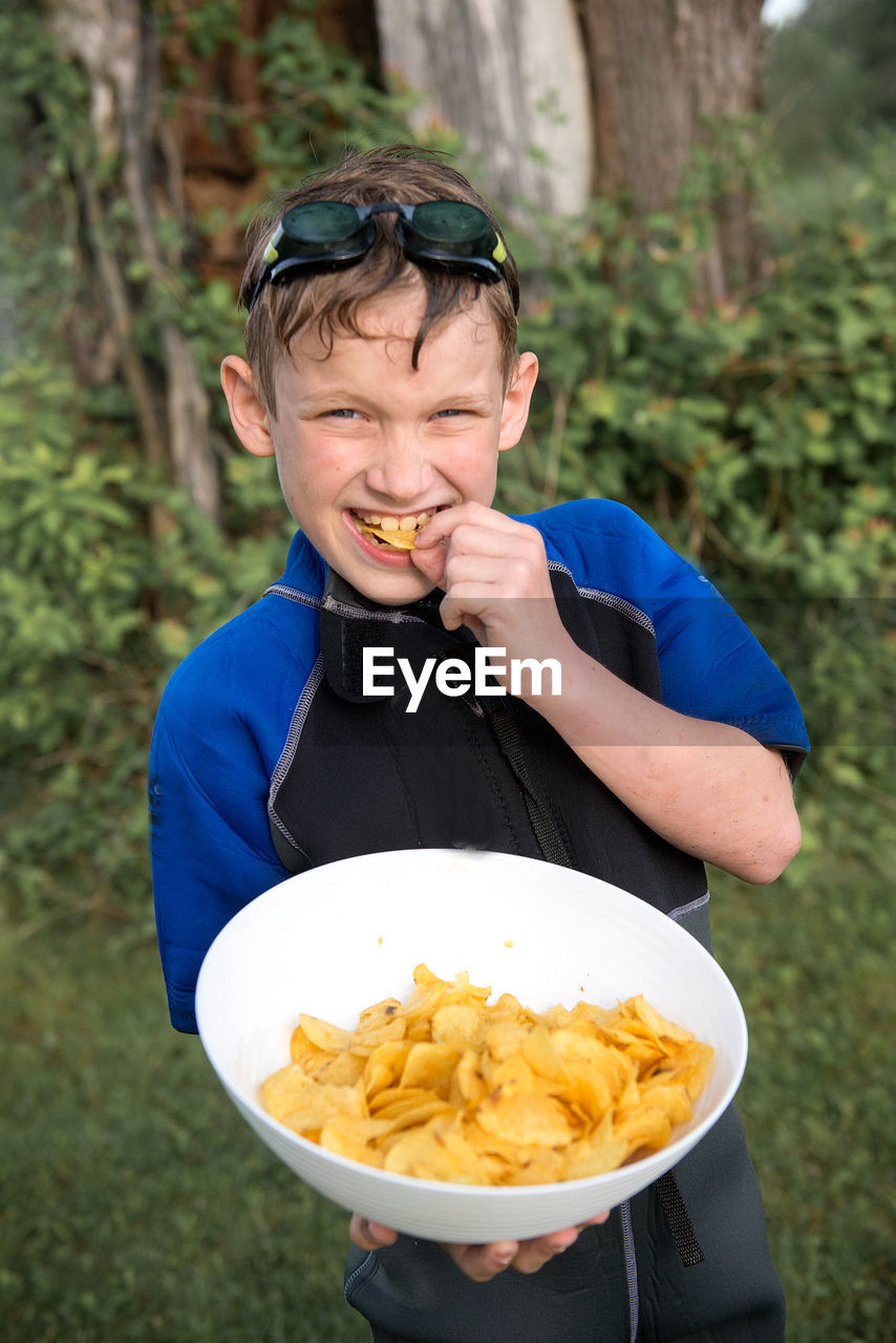 High angle portrait of boy eating potato chips on field