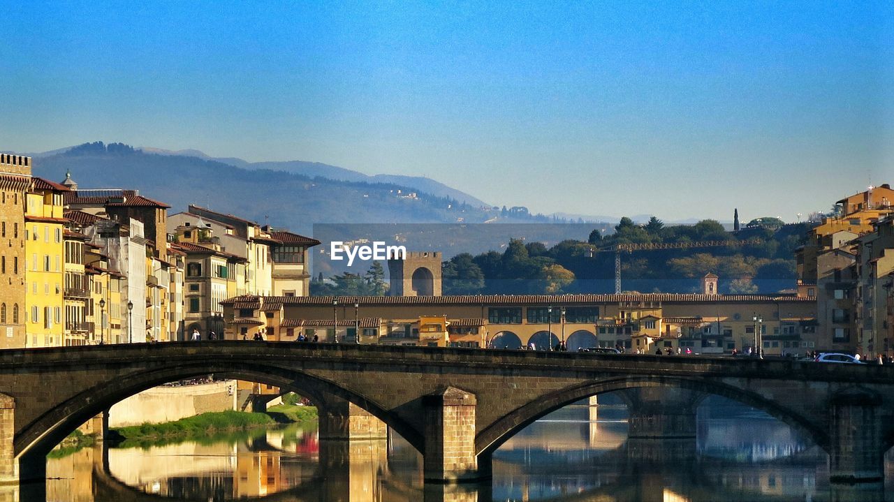 Bridge over river amidst buildings against clear blue sky in city