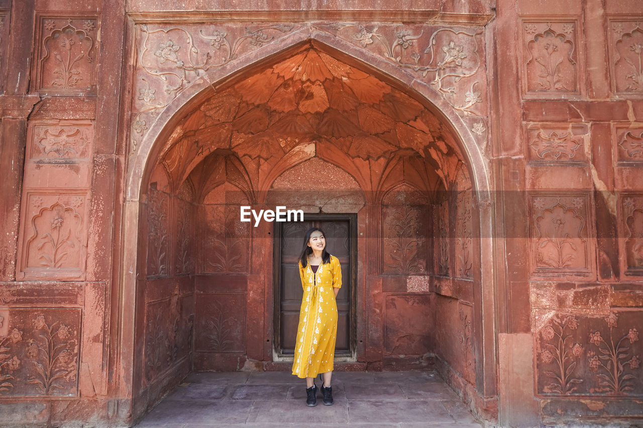 Ethnic young barefoot woman in traditional clothes walking and looking at camera against aged arch door in the red fort in new delhi, india