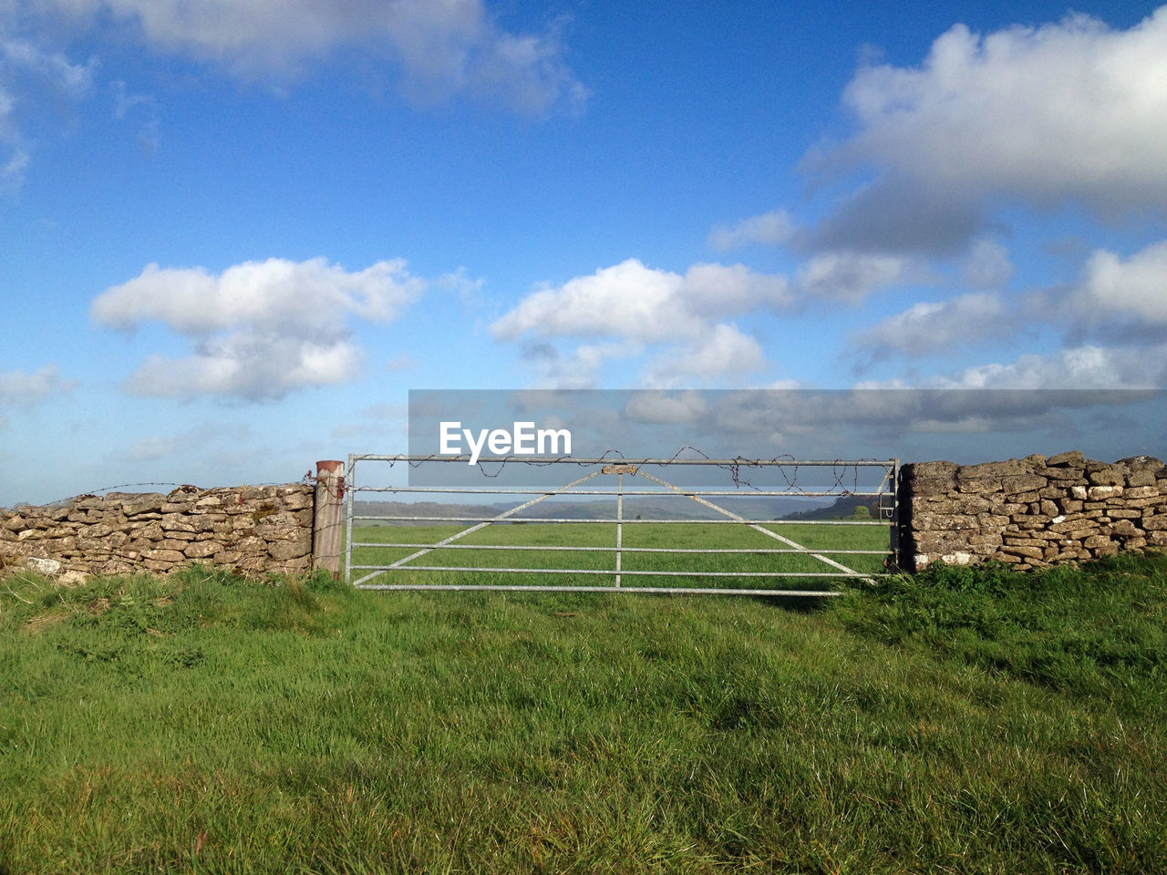 Closed gate on grassy field against sky