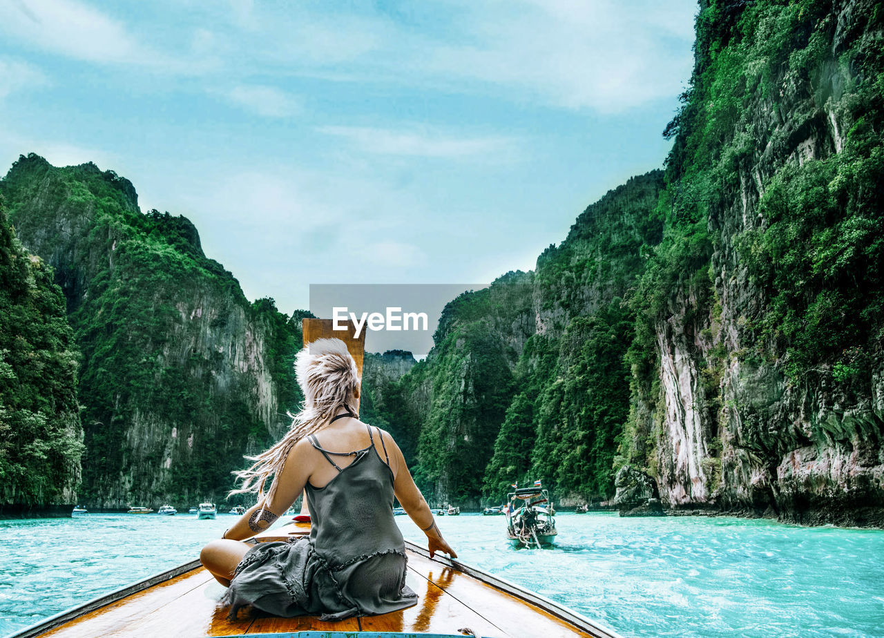 Rear view of woman sitting on boat by sea against sky