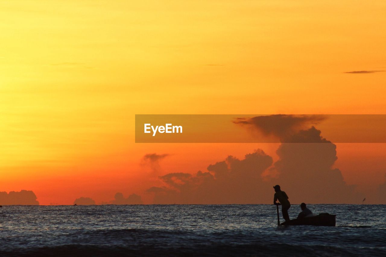 Silhouette people in boat on lake against sky during sunset