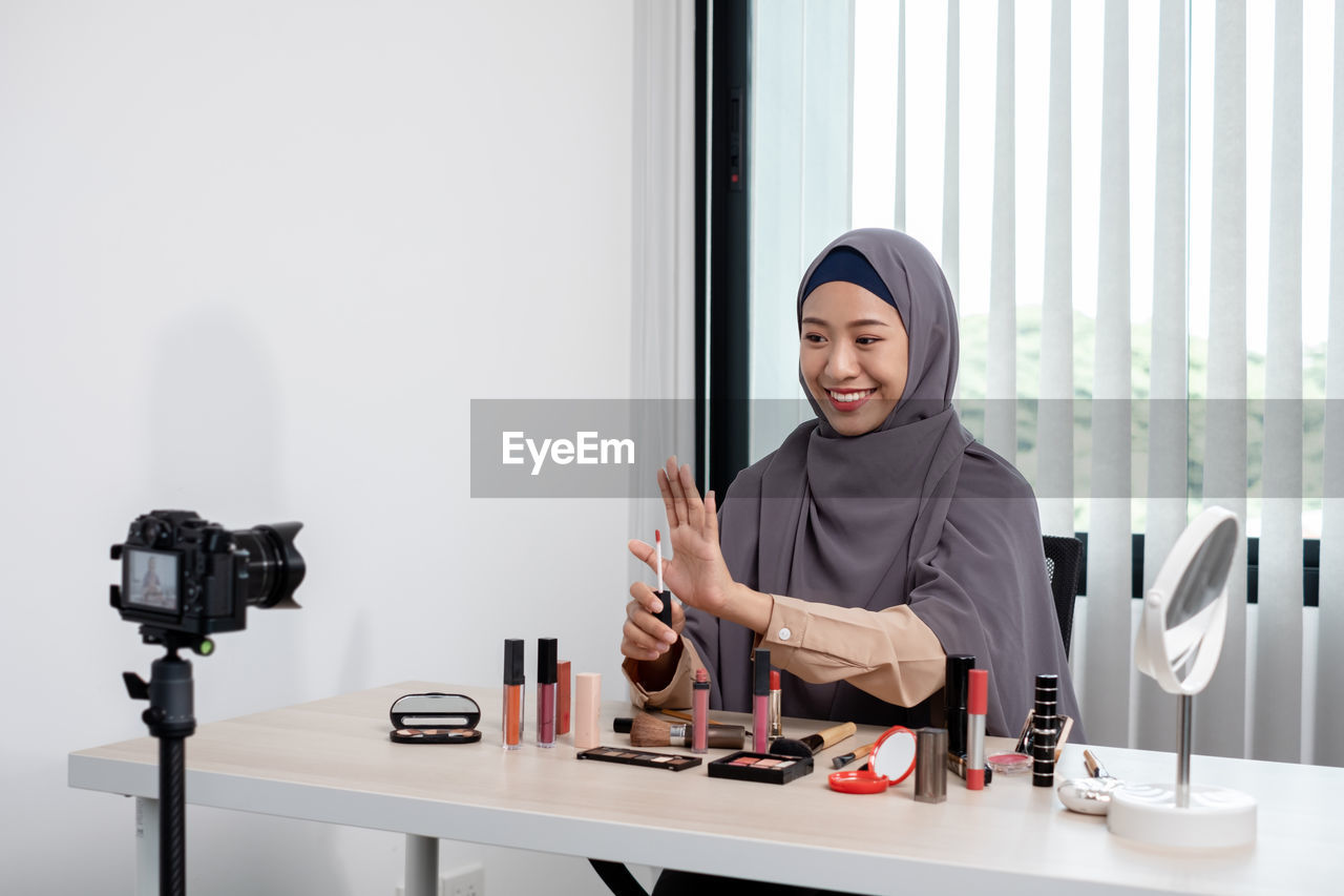 Young woman blogging while applying make up at office