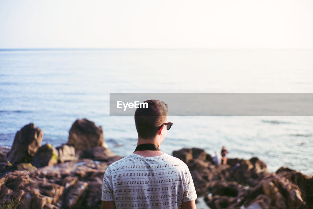 REAR VIEW OF MAN LOOKING AT SEA SHORE